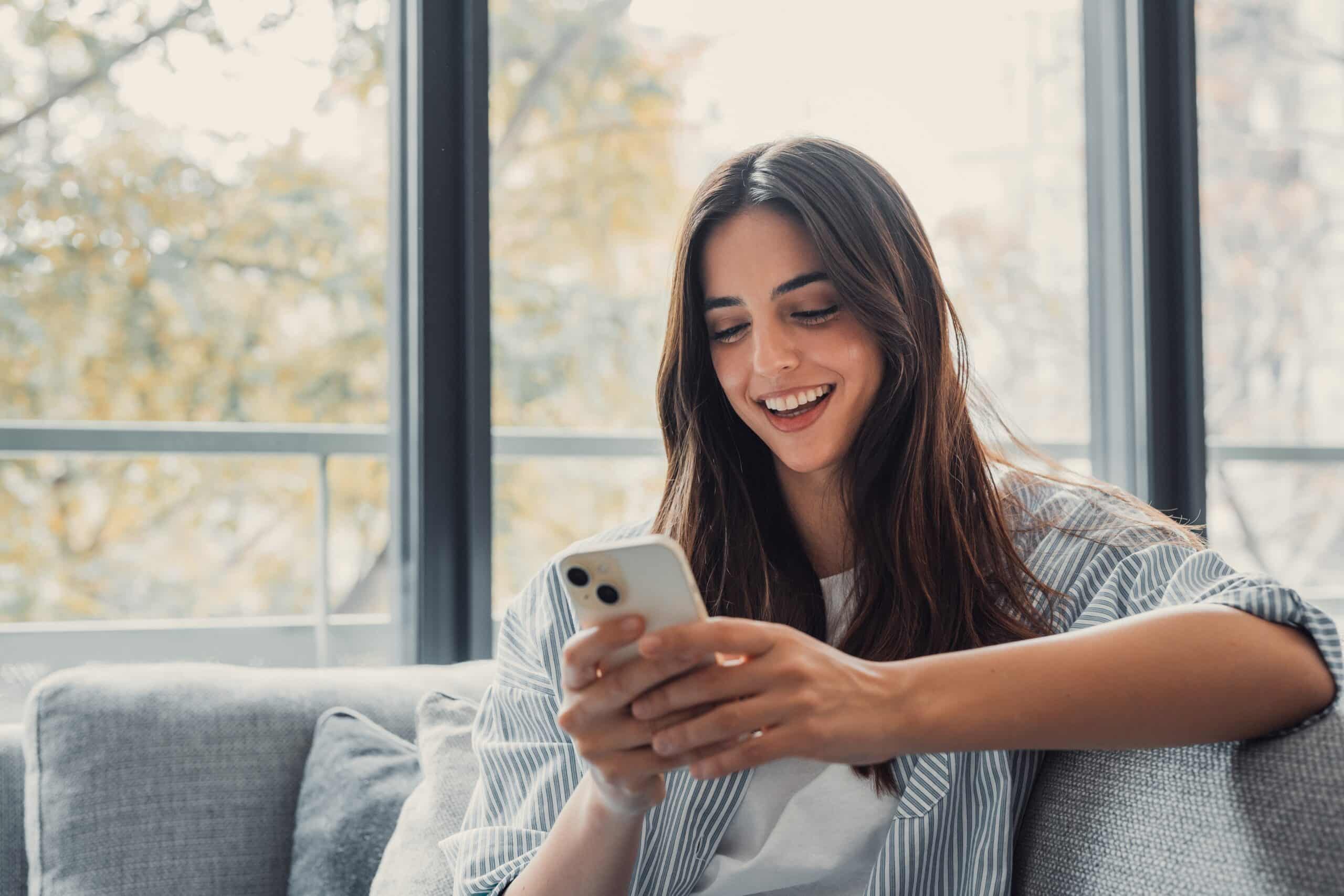 Happy,Pleasant,Millennial,Woman,Relaxing,On,Comfortable,Couch,,Holding,Smartphone